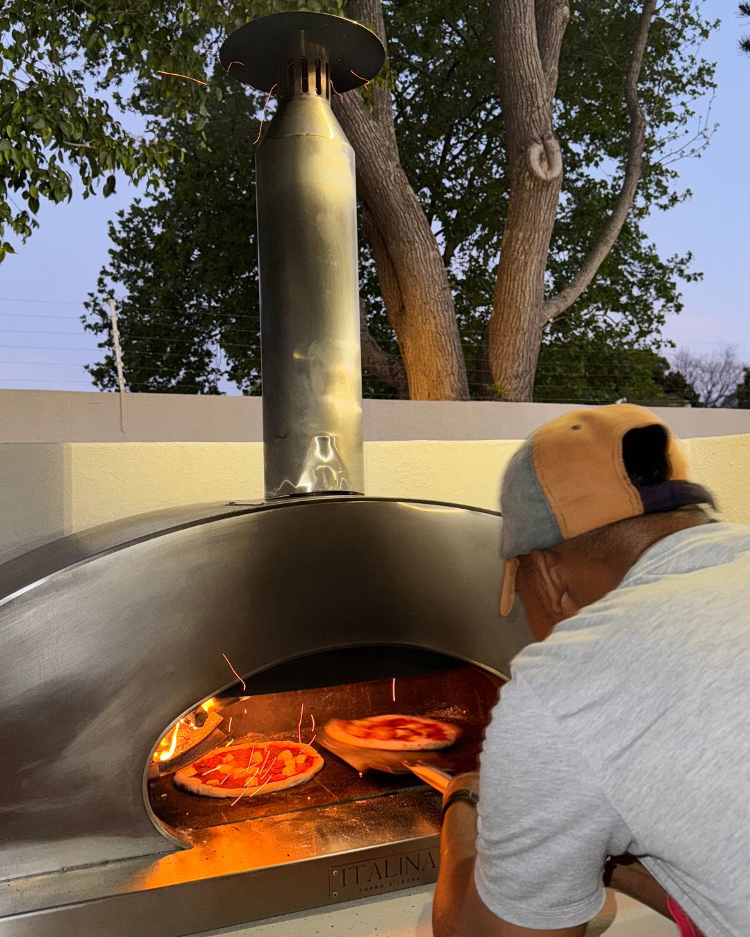 Pizzas being turned inside the Italina wood-fired oven at dusk